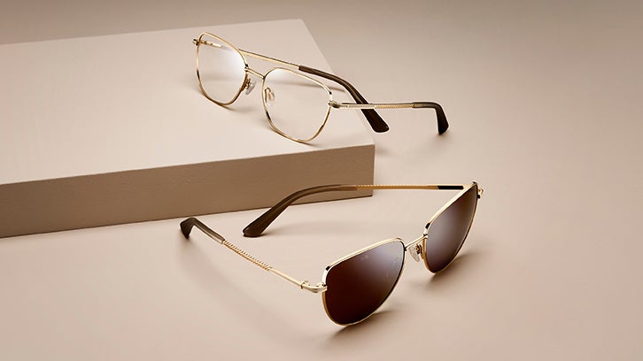 Gold eyeglasses and sunglasses displayed on a neutral pedestal.